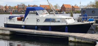 Witte boot met blauwe romp en buiskap, aangemeerd aan steiger.