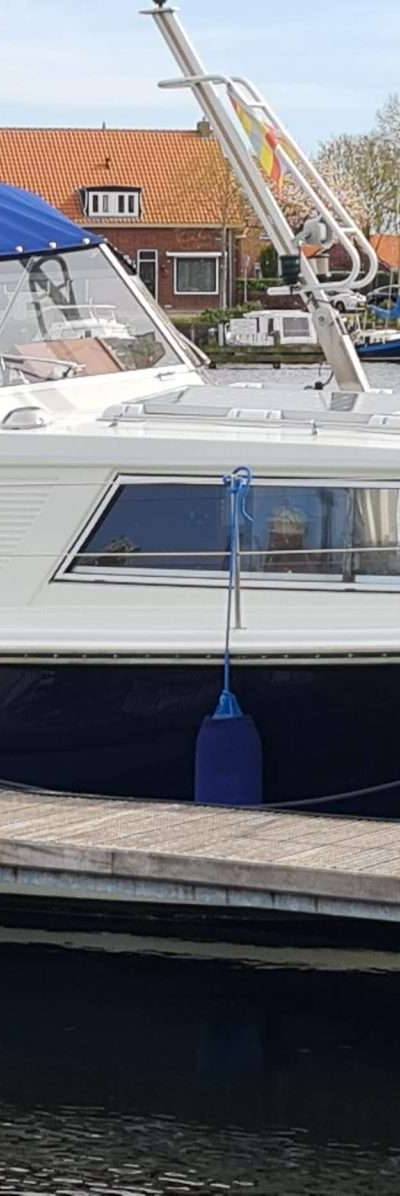 Witte boot met blauwe romp en buiskap, aangemeerd aan steiger.
