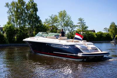 Luxe motorboot op water, met stuurman, varend onder Nederlandse vlag.