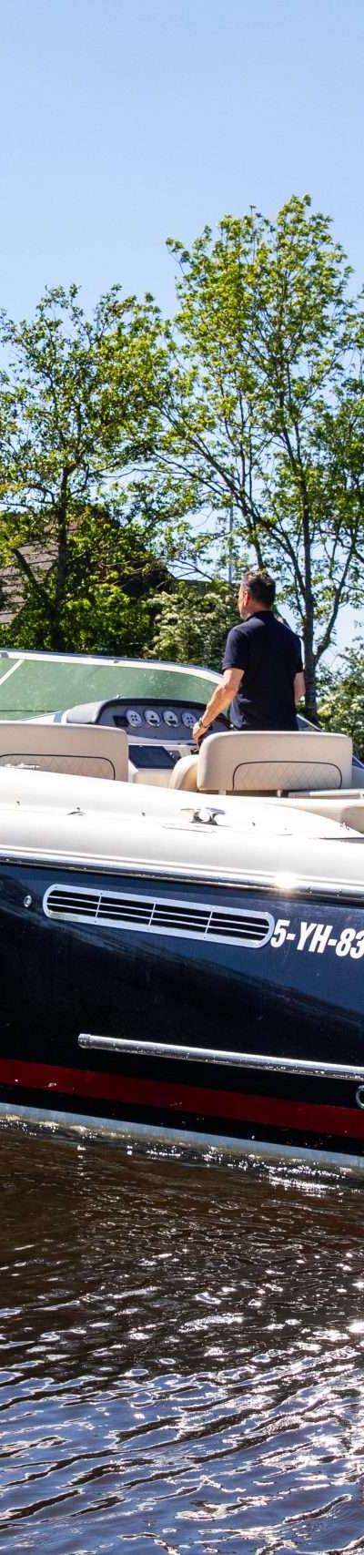 Luxe motorboot op water, met stuurman, varend onder Nederlandse vlag.