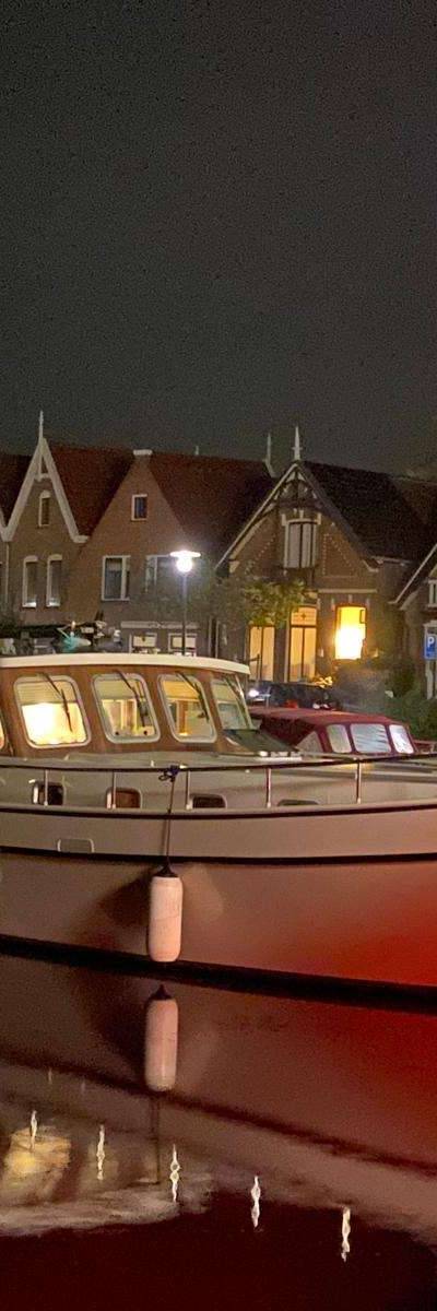 Boot 'Drechtstaete' aan nachtelijke kade, verlichte huizen spiegelen in water.