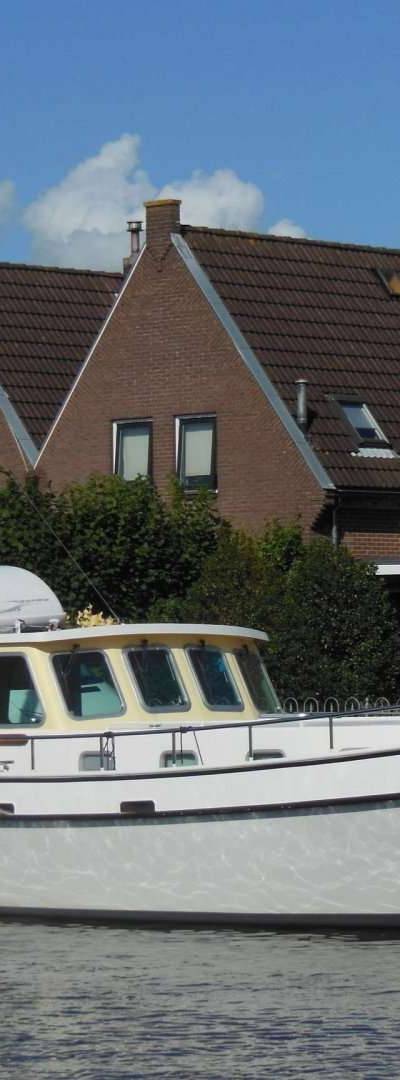 Witte stalen boot met ramen en relingen, liggend voor huizenrij.