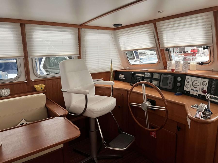 Stuurstand met wit lederen stoel, houten stuurwiel en navigatieapparatuur.