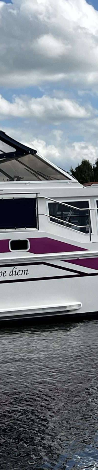 Een witte motorboot met paarse accenten ligt afgemeerd in het water.