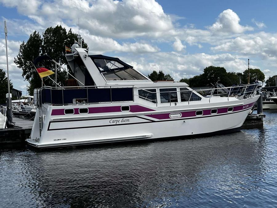 Een witte motorboot met paarse accenten ligt afgemeerd in het water.