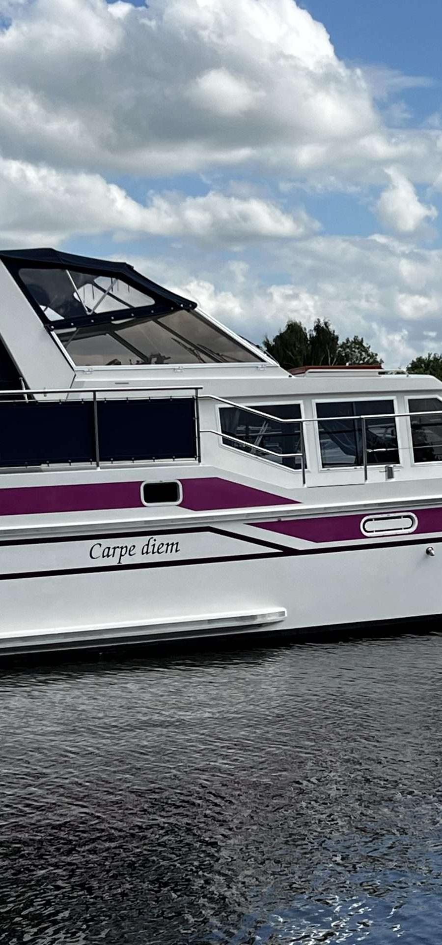 Een witte motorboot met paarse accenten ligt afgemeerd in het water.