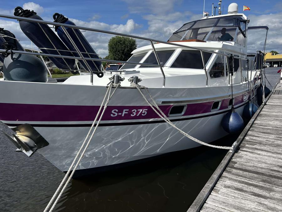 Witte jacht met paarse streep, deels aangelegd aan steiger.