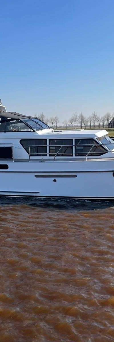 Motorjacht in kanaal met Nederlandse vlag en landschap